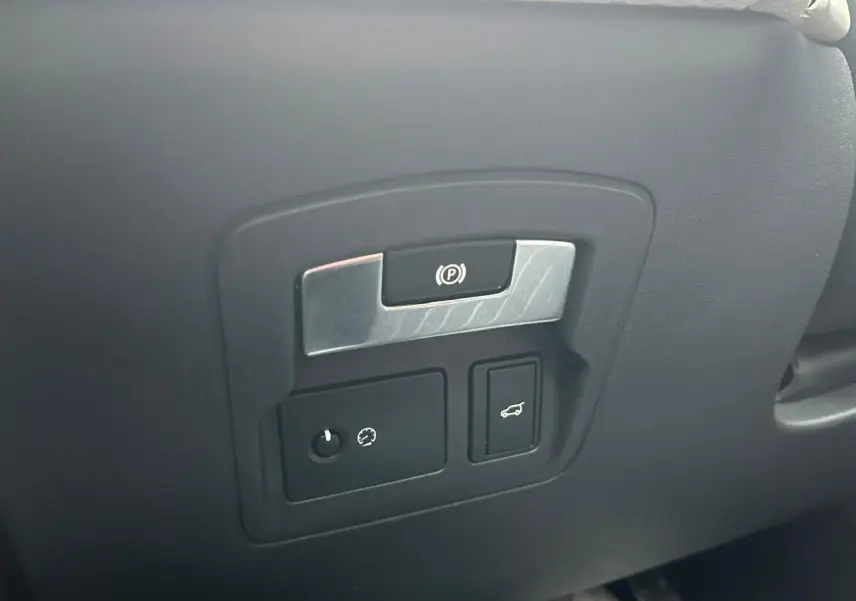 Détail du tableau de bord noir avec commandes de frein à main électrique et ouverture du hayon sur Range Rover Velar gris Ammonite.