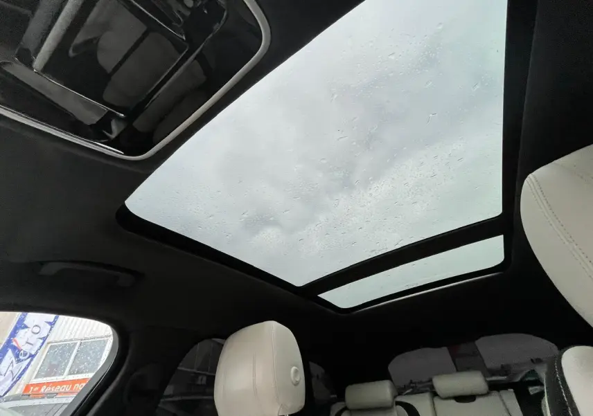 Vue intérieure du toit ouvrant panoramique et des sièges clairs du Range Rover Velar gris Ammonite, ambiance lumineuse naturelle.