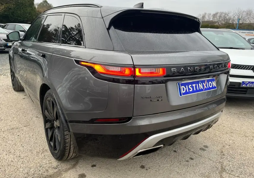 Vue 3/4 arrière droite d’un Range Rover Velar gris ammonite avec jantes noires 21 pouces et feux arrière allumés.