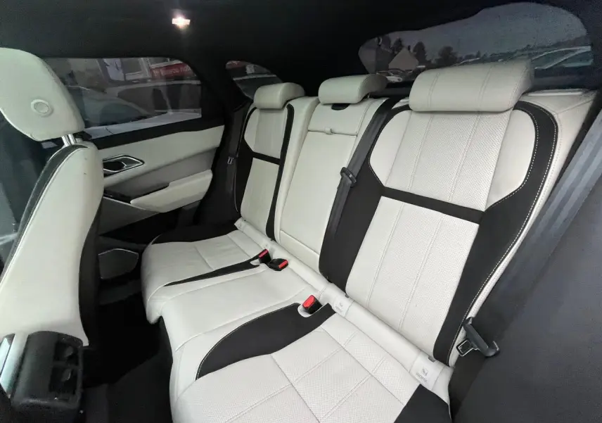 Vue intérieure côté droit sur la banquette arrière cuir blanc et noir du Range Rover Velar avec appuie-tête et ceintures visibles.