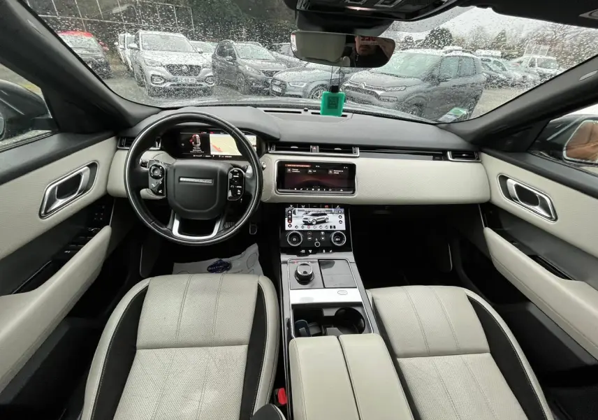 Vue intérieure avant du Range Rover Velar 2017, sièges cuir clair, tableau de bord moderne avec double écran tactile.