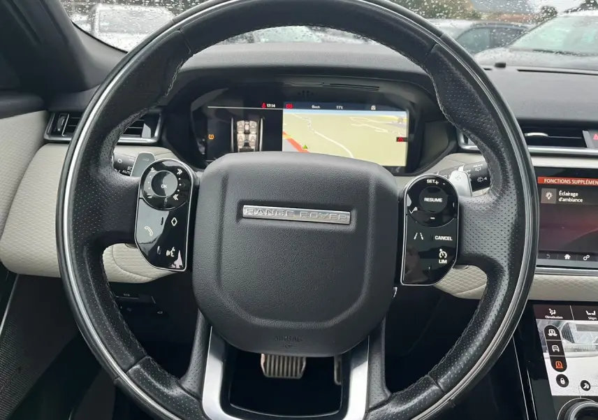 Vue rapprochée du volant cuir perforé noir du Range Rover Velar avec commandes intégrées et écran de navigation digital.