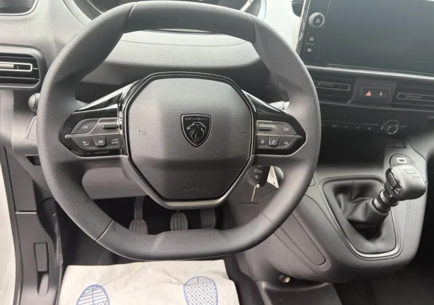 Vue intérieure centrée sur le volant cuir multifonctions et levier de vitesses manuel du Peugeot Partner blanc 2026.