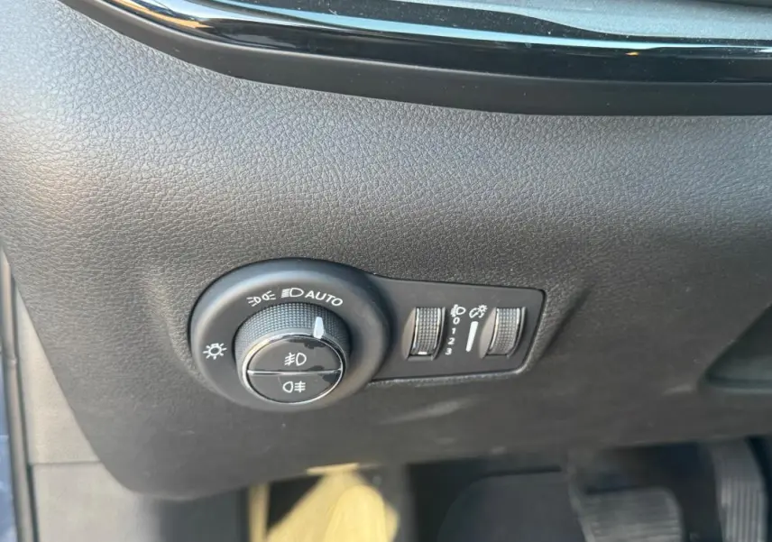 Gros plan sur les commandes d’éclairage du tableau de bord du Jeep Compass bleu, avec molette de réglage des phares et boutons adjacents.