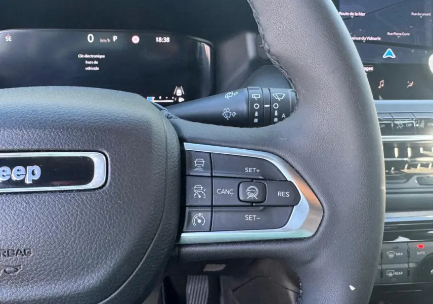 Gros plan sur le volant noir du Jeep Compass 2025 avec commandes au volant et tableau de bord numérique en arrière-plan.