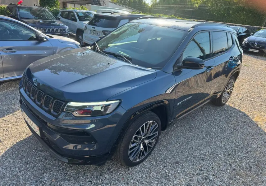 Jeep Compass bleu en vue 3/4 avant droit, avec jantes alliage 19 pouces et barres de toit visibles.