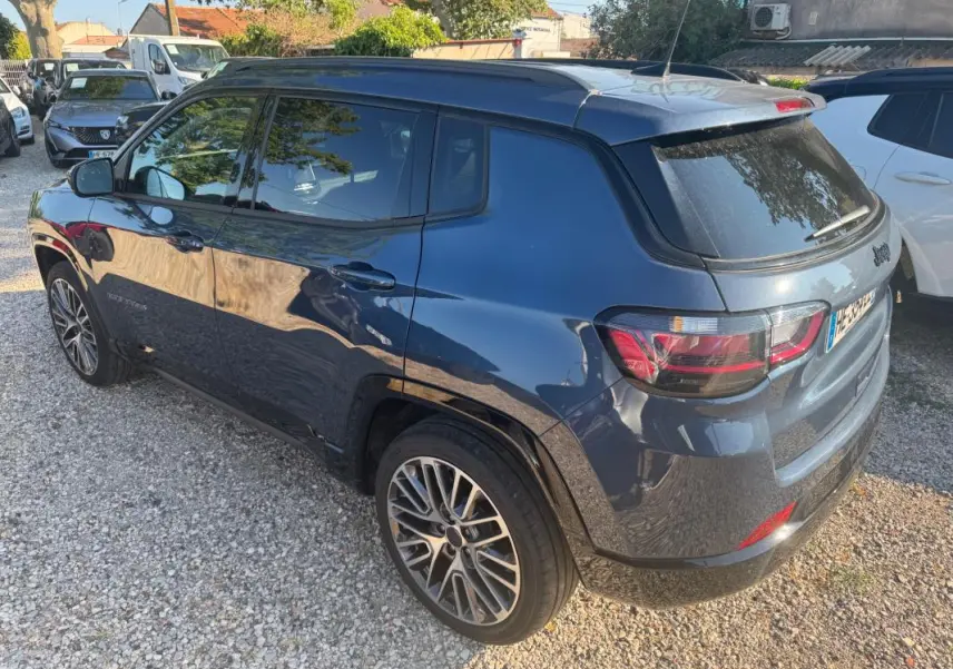 Jeep Compass bleu vue 3/4 arrière côté gauche, avec jantes alliage 19 pouces et barres de toit visibles.