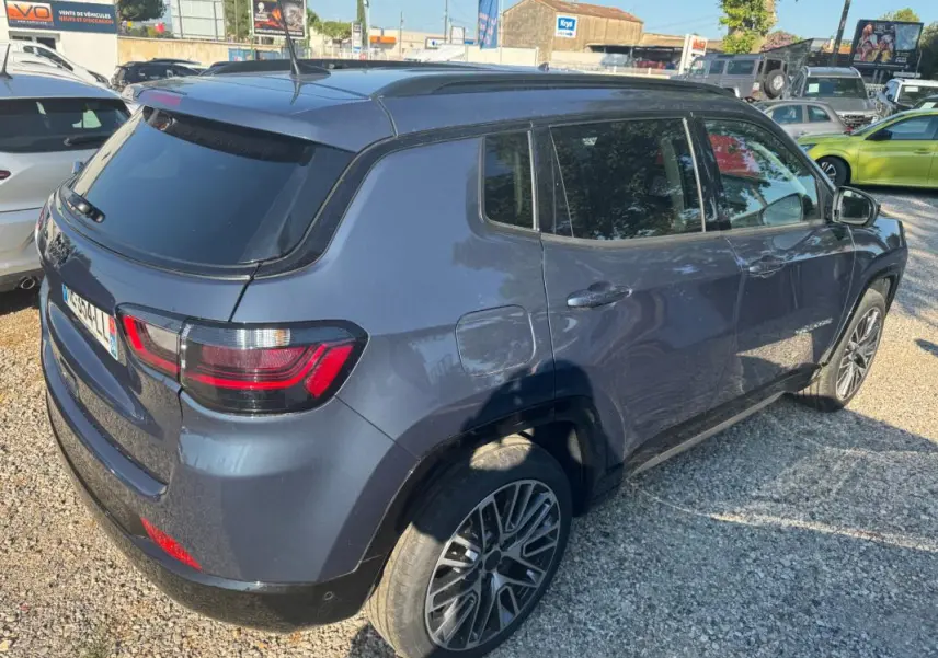 Jeep Compass bleu en 3/4 arrière droit, avec jantes alliage 19 pouces et barres de toit visibles.