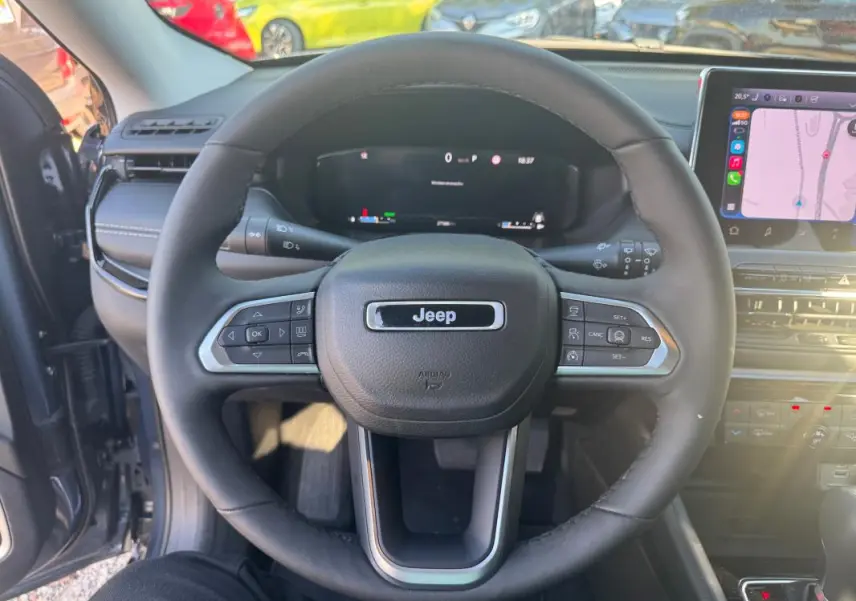 Vue intérieure centrée sur le volant Jeep noir du Compass 2025 avec tableau de bord numérique et écran tactile visible.