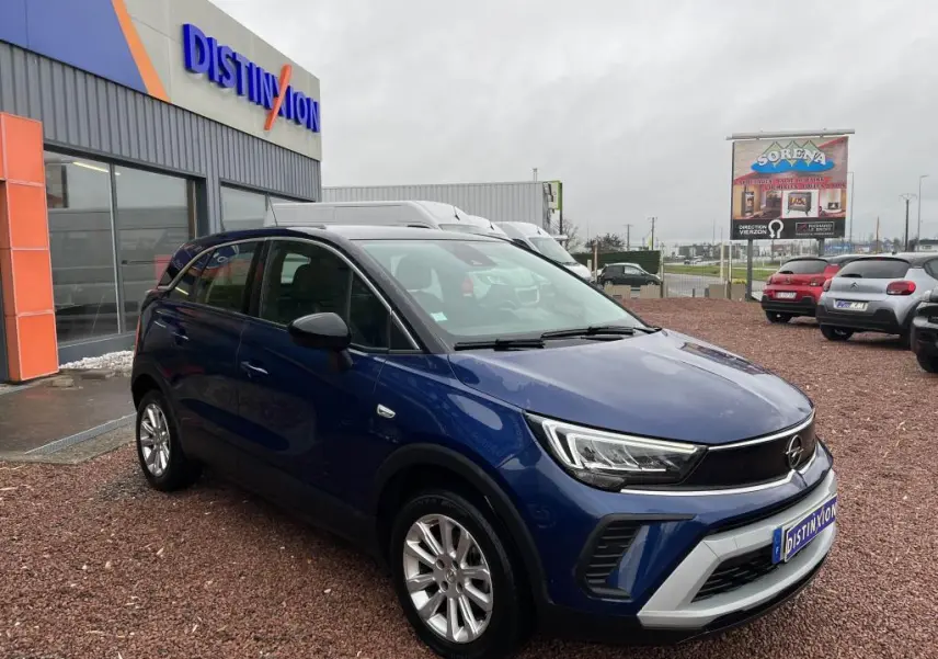 Opel Crossland X bleu clair en 3/4 avant droit avec toit noir, stationné devant un bâtiment commercial.