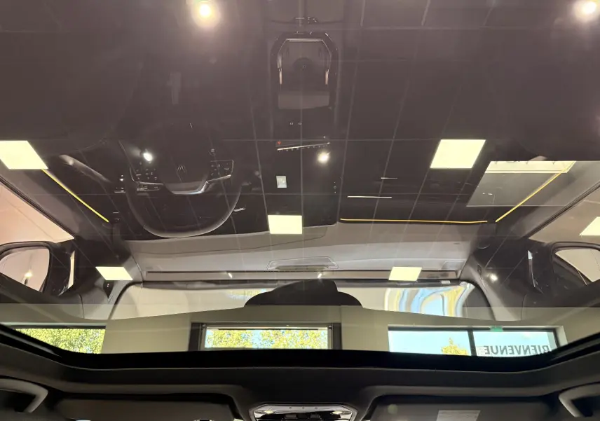 Vue intérieure du toit panoramique noir du Renault Austral blanc nacré, avec reflet du plafond et du volant.