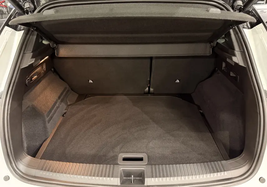 Coffre ouvert vu de l'arrière d'un Renault Austral blanc nacré avec intérieur de coffre noir et cache-bagages déployé.
