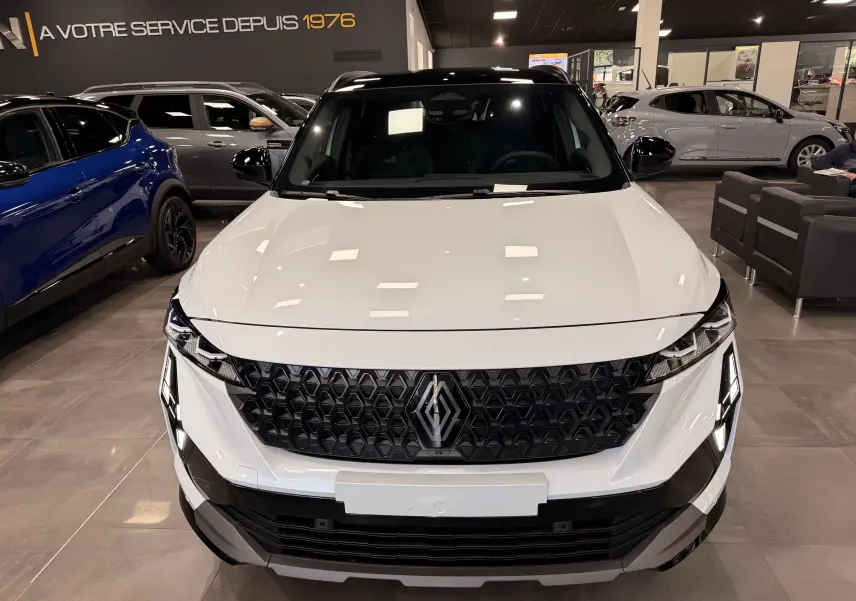 Vue de face du Renault Austral blanc nacré avec toit noir, mettant en valeur sa calandre hexagonale distinctive en showroom.