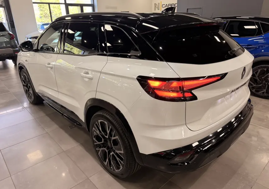 Vue 3/4 arrière droite du Renault Austral blanc nacré avec toit noir et feux arrière allumés en intérieur showroom.