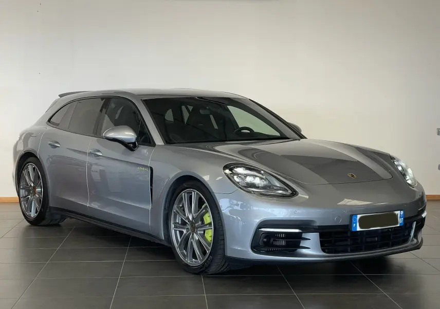 Porsche Panamera Sport Turismo gris en 3/4 avant gauche, avec jantes alliage et étriers de frein verts hybrides visibles.