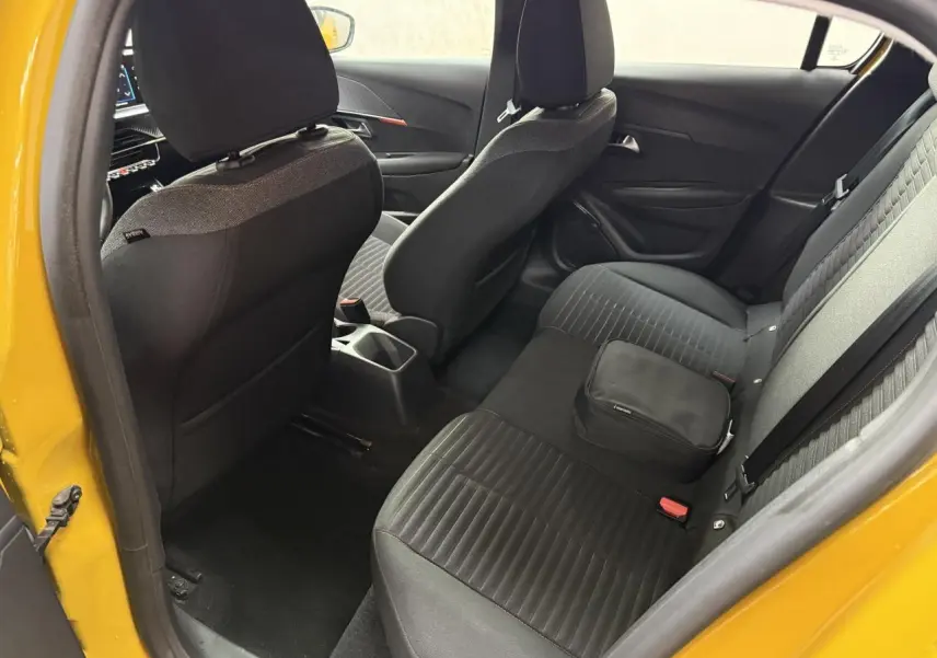Vue intérieure arrière droite d'une Peugeot 208 jaune clair, montrant les sièges noirs et un sac posé sur la banquette.