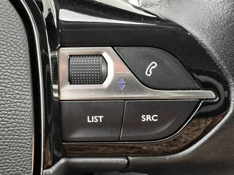 Gros plan sur les commandes noires du volant multifonction du Peugeot 2008 blanc banquise, avec molette et boutons SRC et LIST.