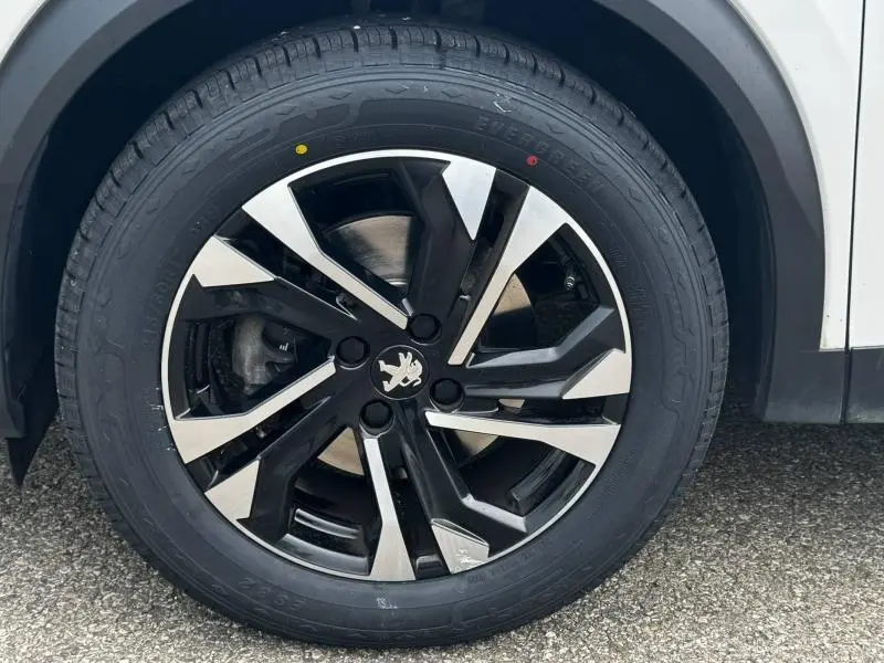 Gros plan sur la roue avant droite du Peugeot 2008 blanc banquise, mettant en valeur la jante alu noire et argentée au design moderne.