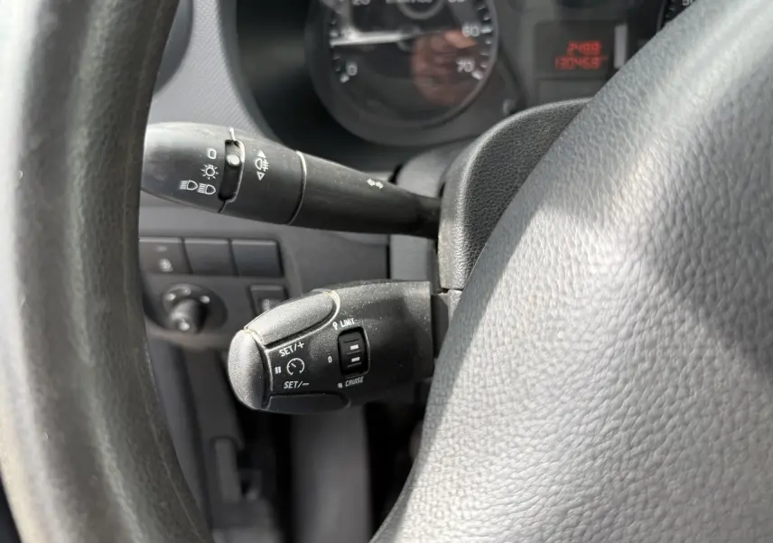 Gros plan sur le volant et les commandes de régulateur de vitesse du Peugeot Partner blanc, version 2017, intérieur tissu noir.