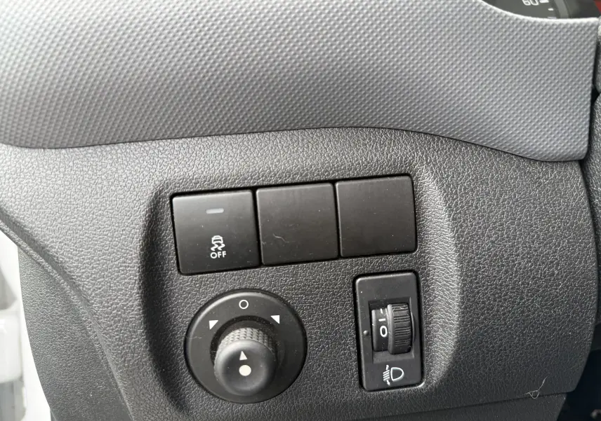 Gros plan sur les commandes de réglage des rétroviseurs et des phares du tableau de bord d’un Peugeot Partner blanc de 2017.