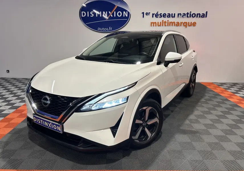 Nissan Qashqai blanc lunaire en 3/4 avant droit, avec toit panoramique et phares LED allumés dans un showroom.
