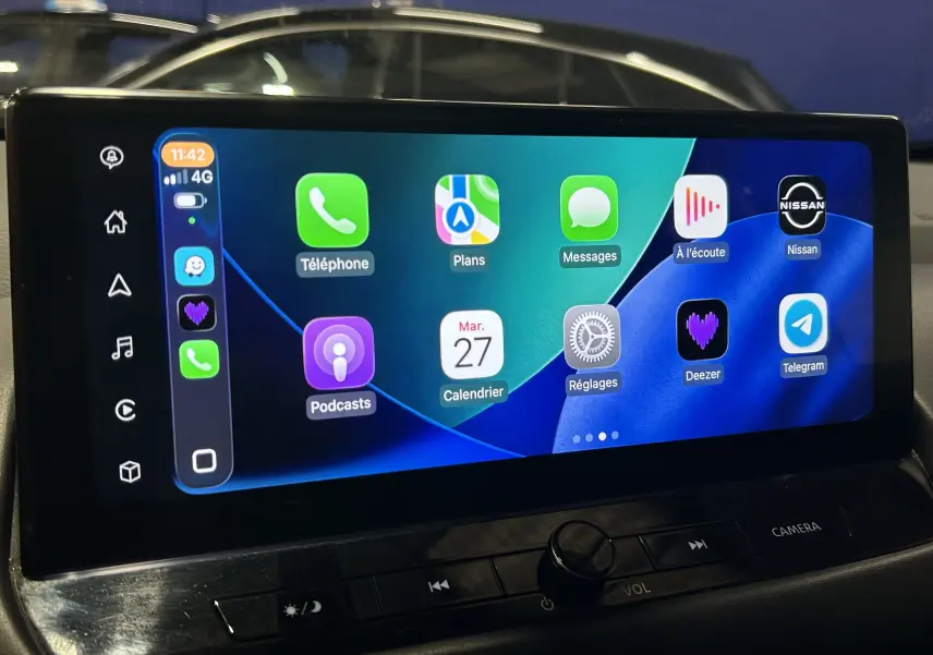 Écran tactile central du Nissan Qashqai 2023 affichant Apple CarPlay avec commandes audio et bouton caméra visible.