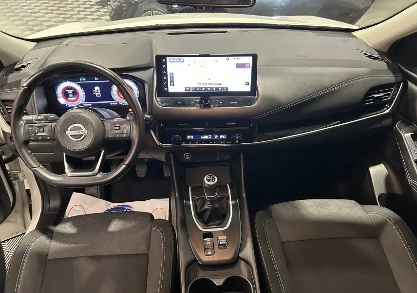 Vue intérieure frontale du Nissan Qashqai blanc lunaire 2023, avec tableau de bord numérique et boîte manuelle.