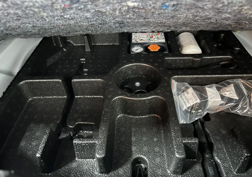 Gros plan sur le rangement en mousse noir sous le coffre du Nissan Qashqai blanc lunaire, avec accessoires et notice visibles.