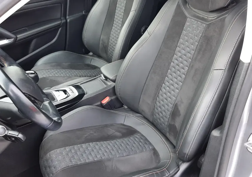 Vue intérieure de face des sièges avant en tissu noir et alcantara d'une Peugeot 308 SW gris Artense, avec coutures apparentes.