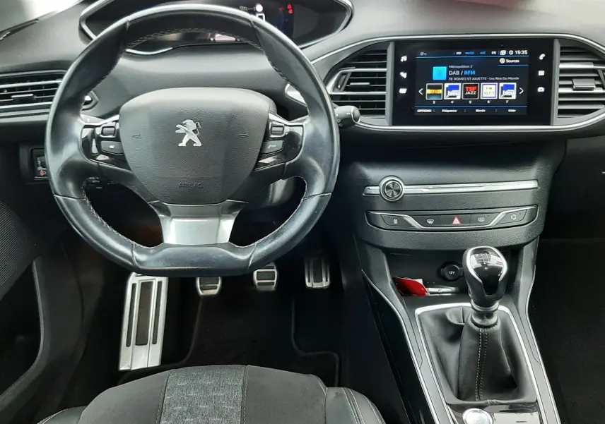 Vue intérieure frontale du poste de conduite de la Peugeot 308 SW 2021, volant cuir noir et écran tactile central allumé.