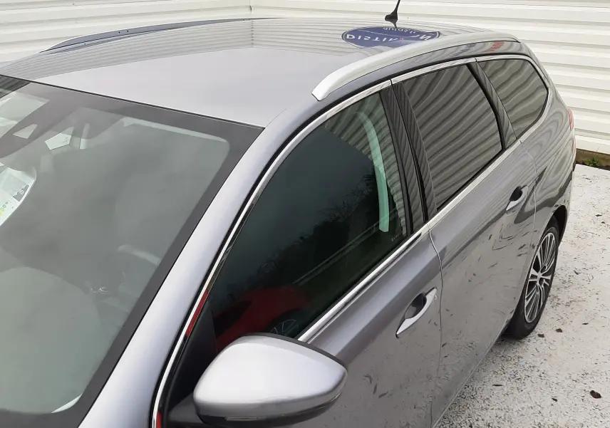 Vue 3/4 avant droit d'une Peugeot 308 SW gris Artense avec barres de toit et vitres teintées.