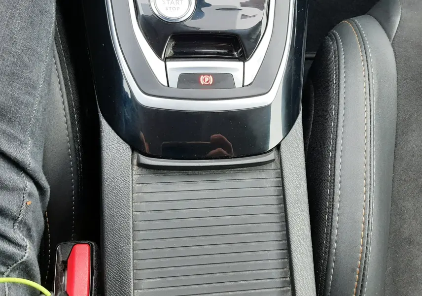 Vue plongeante sur la console centrale noire brillante de la Peugeot 308 SW 1.2 PureTech avec bouton start/stop et frein à main électronique.
