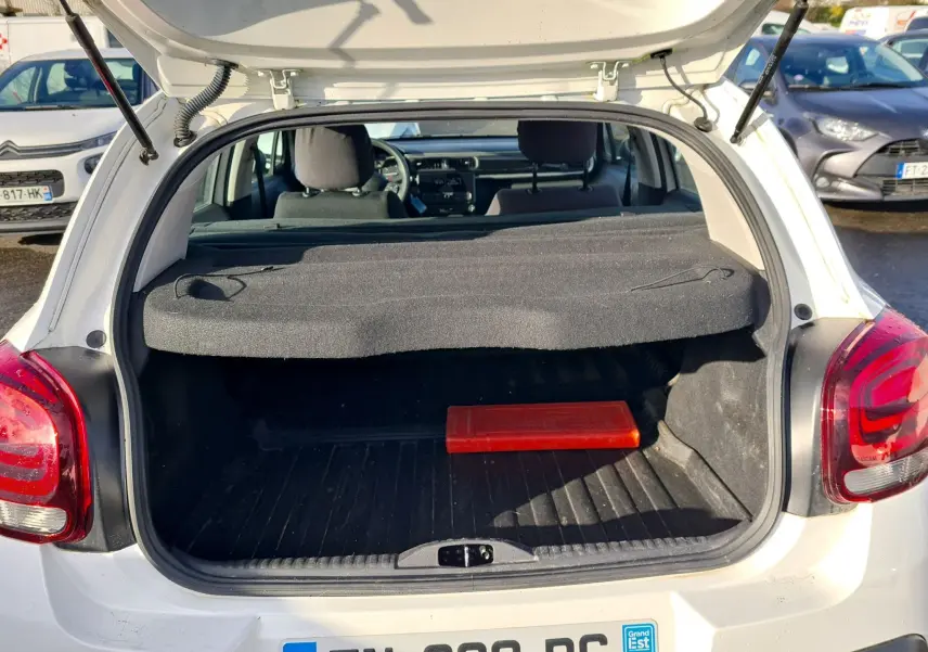 Coffre ouvert vu de l’arrière d’une Citroën C3 Société blanche 2020 avec cache-bagages et triangle de signalisation rouge.