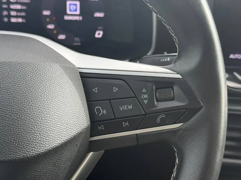 Gros plan sur les commandes multifonctions du volant cuir du SEAT LEON blanc Nevada 2025, boutons de navigation et appel.