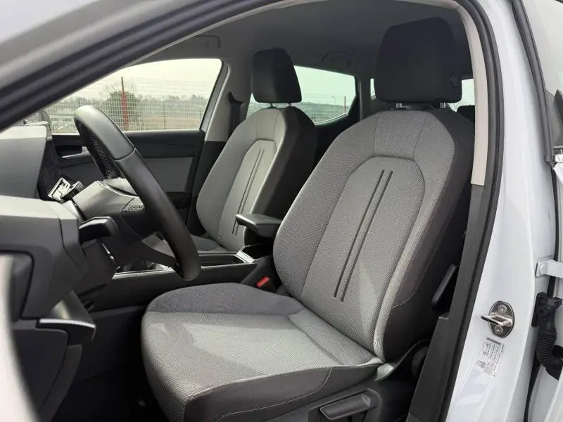 Vue intérieure côté conducteur de la SEAT LEON 2025 blanche avec sièges tissu gris et accoudoir central.