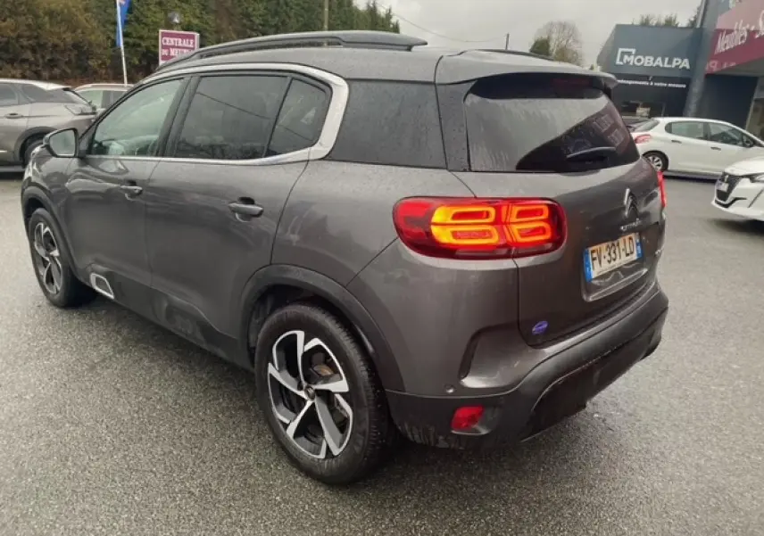 Vue 3/4 arrière droite d'un Citroën C5 Aircross gris platinium avec feux arrière allumés et jantes alliage 18 pouces.