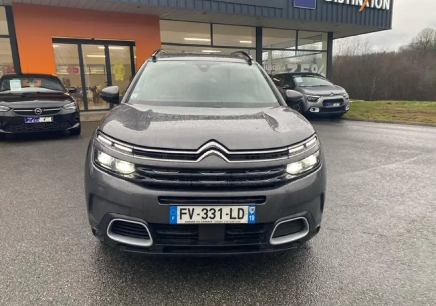 Vue avant d'un Citroën C5 Aircross gris platinium avec phares allumés sur un parking humide.