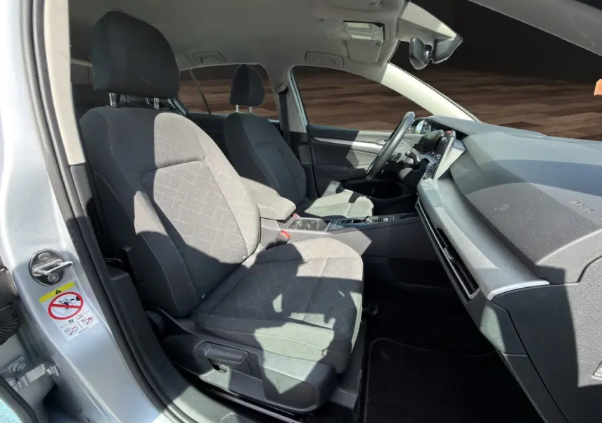 Vue intérieure côté conducteur d'une Volkswagen Golf gris clair 2022, sièges tissu gris et tableau de bord moderne.