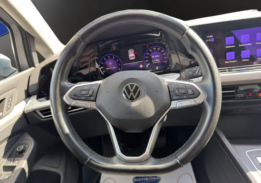 Vue intérieure centrée sur le volant cuir noir et les écrans digitaux du tableau de bord de la Volkswagen Golf gris clair.
