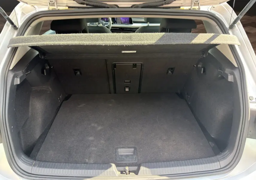 Vue arrière du coffre ouvert d'une Volkswagen Golf gris clair, montrant l'espace de chargement vide et la tablette de coffre relevée.