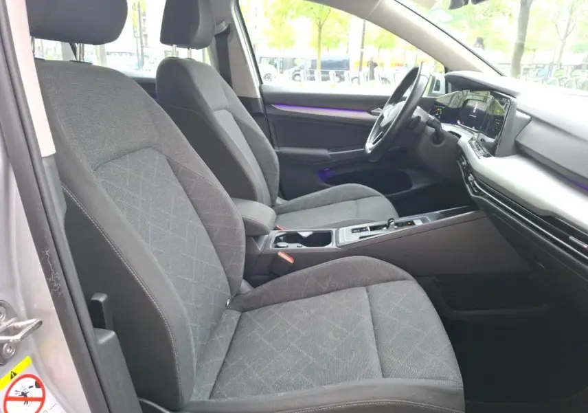 Intérieur de la Volkswagen Golf 1.0 ETSI gris clair, vue côté conducteur, sièges tissu et tableau de bord moderne avec écran tactile.