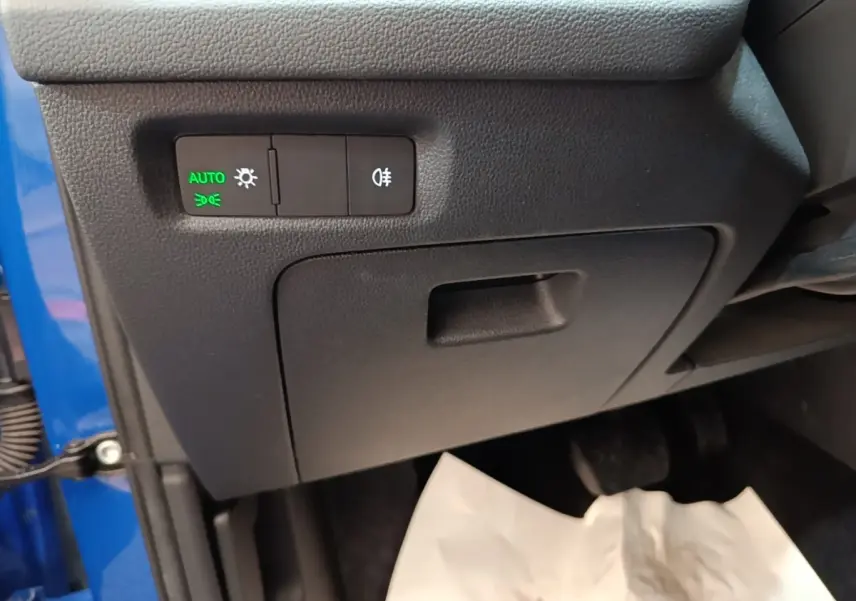 Détail intérieur côté gauche avec commandes d’éclairage activées en vert, partie de la carrosserie bleue visible.