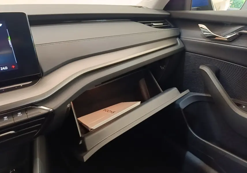 Intérieur de la Skoda Octavia 2024, vue côté passager sur la boîte à gants ouverte avec manuel visible, finition noire.