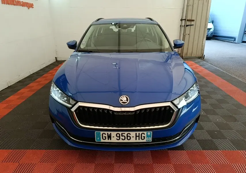 Vue avant d'une Skoda Octavia 2024 bleue avec calandre noire et phares LED, stationnée en intérieur sur sol à damier rouge et noir.