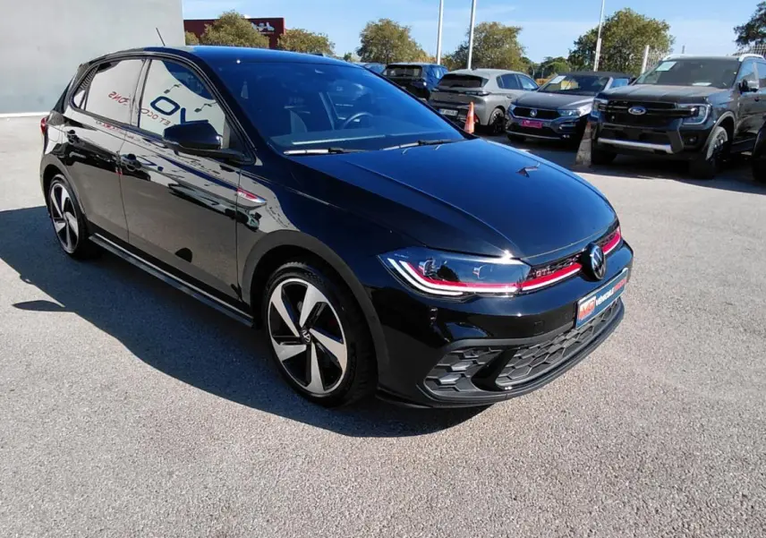 Volkswagen Polo GTI noire vue 3/4 avant droit avec jantes alliage 17 pouces et bande rouge distinctive.