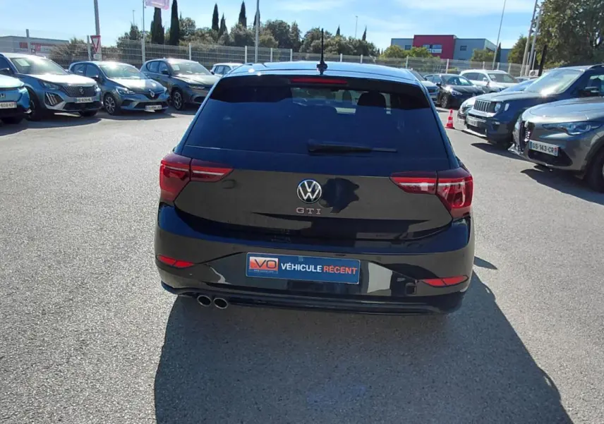 Vue arrière d'une Volkswagen Polo GTI noire 2024 avec double sortie d'échappement et vitres teintées, stationnée en extérieur.