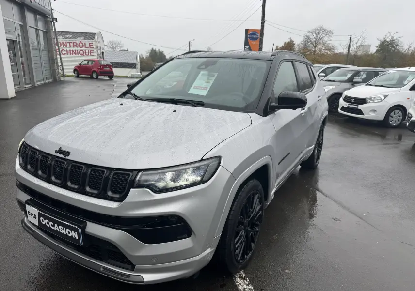 Jeep Compass gris 3/4 avant droit sous la pluie avec calandre noire et jantes foncées visibles.