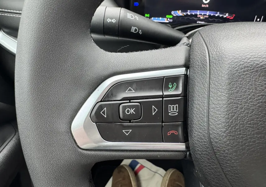 Gros plan sur les commandes du volant côté gauche du Jeep Compass gris 2023, avec boutons de navigation et appel.