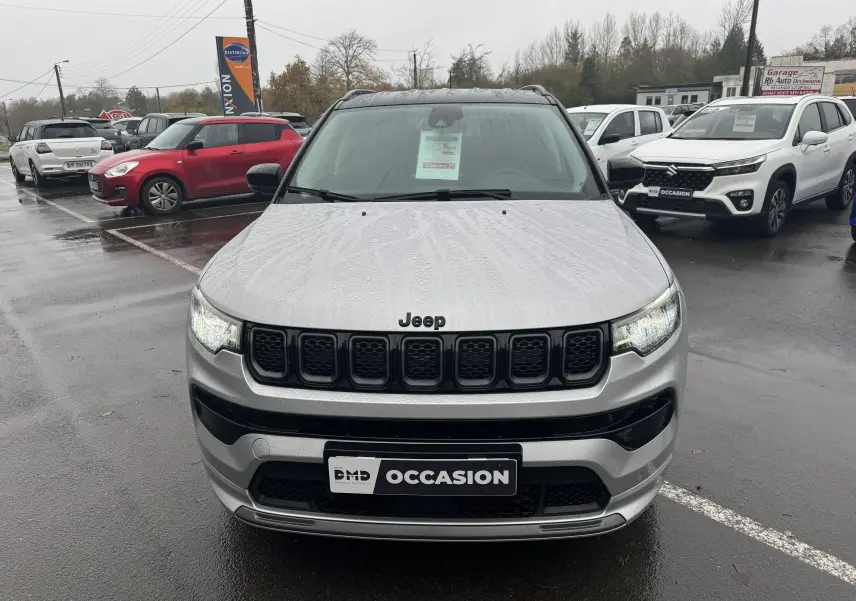 Vue frontale d'un Jeep Compass gris 2023 avec calandre noire et plaque "OCCASION" sur un parking humide.