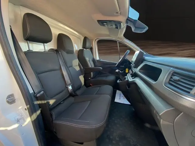 Vue intérieure côté gauche du Renault Trafic Fourgon blanc 2023, montrant les sièges avant en tissu noir et le tableau de bord.